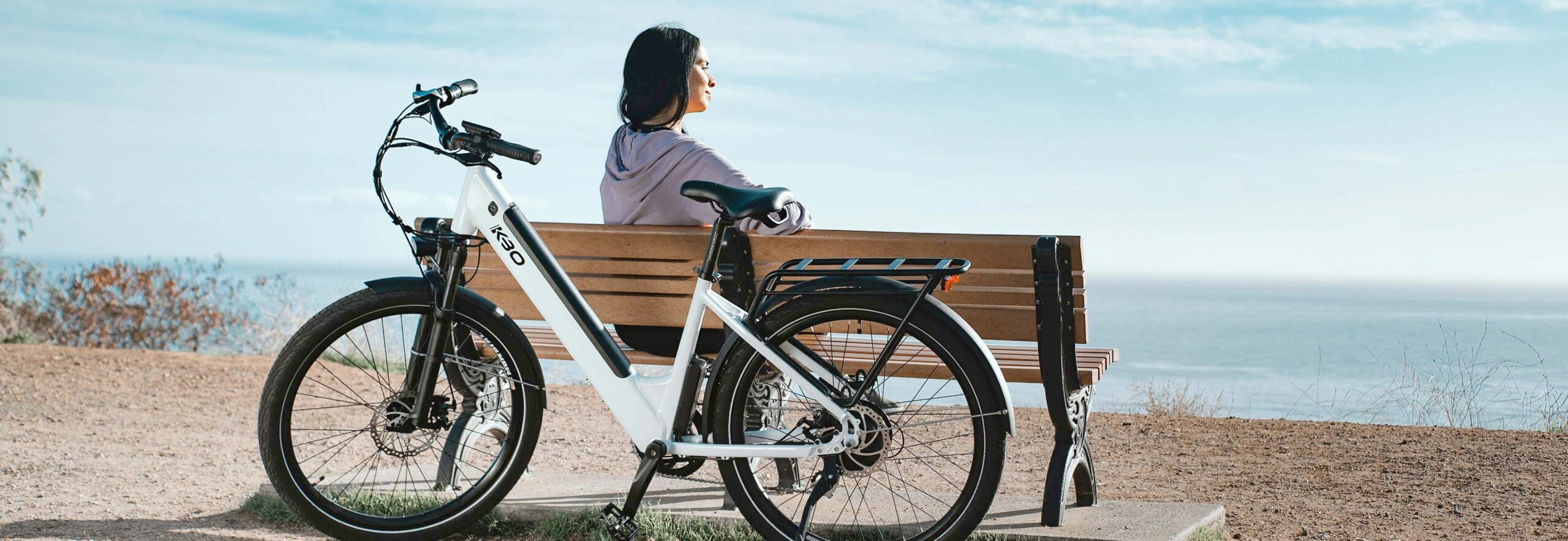 Woman Sitting on Bench with Electric Bike Behind Her Woman Sitting on Bench with Electric Bike Behind Her