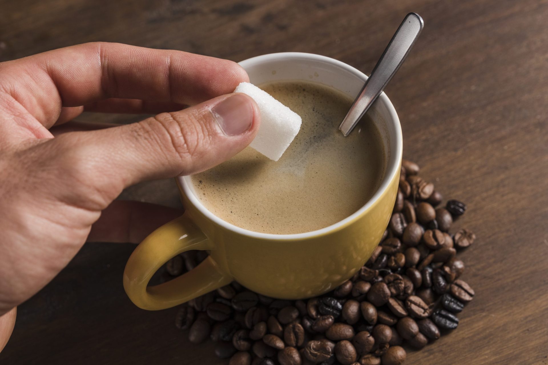 hand-holding-sugar-near-cup-with-coffee